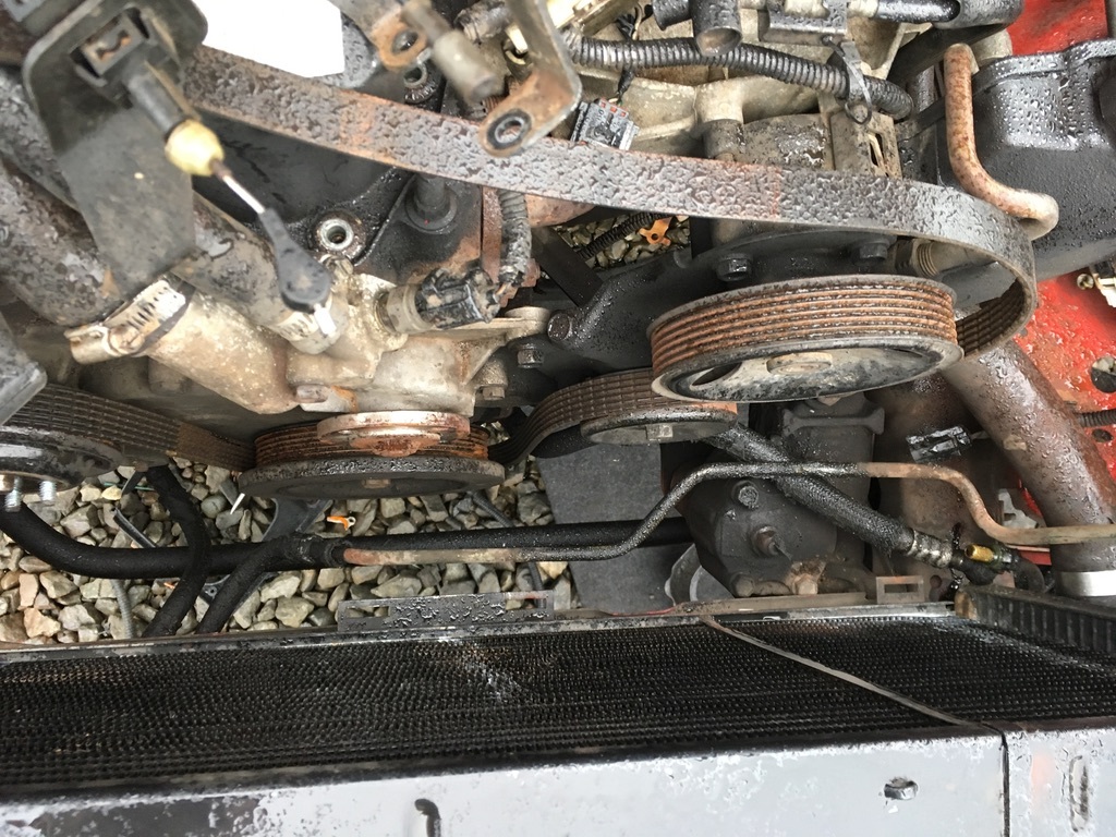 Exposed engine pulleys and belts beside the radiator during a repair.