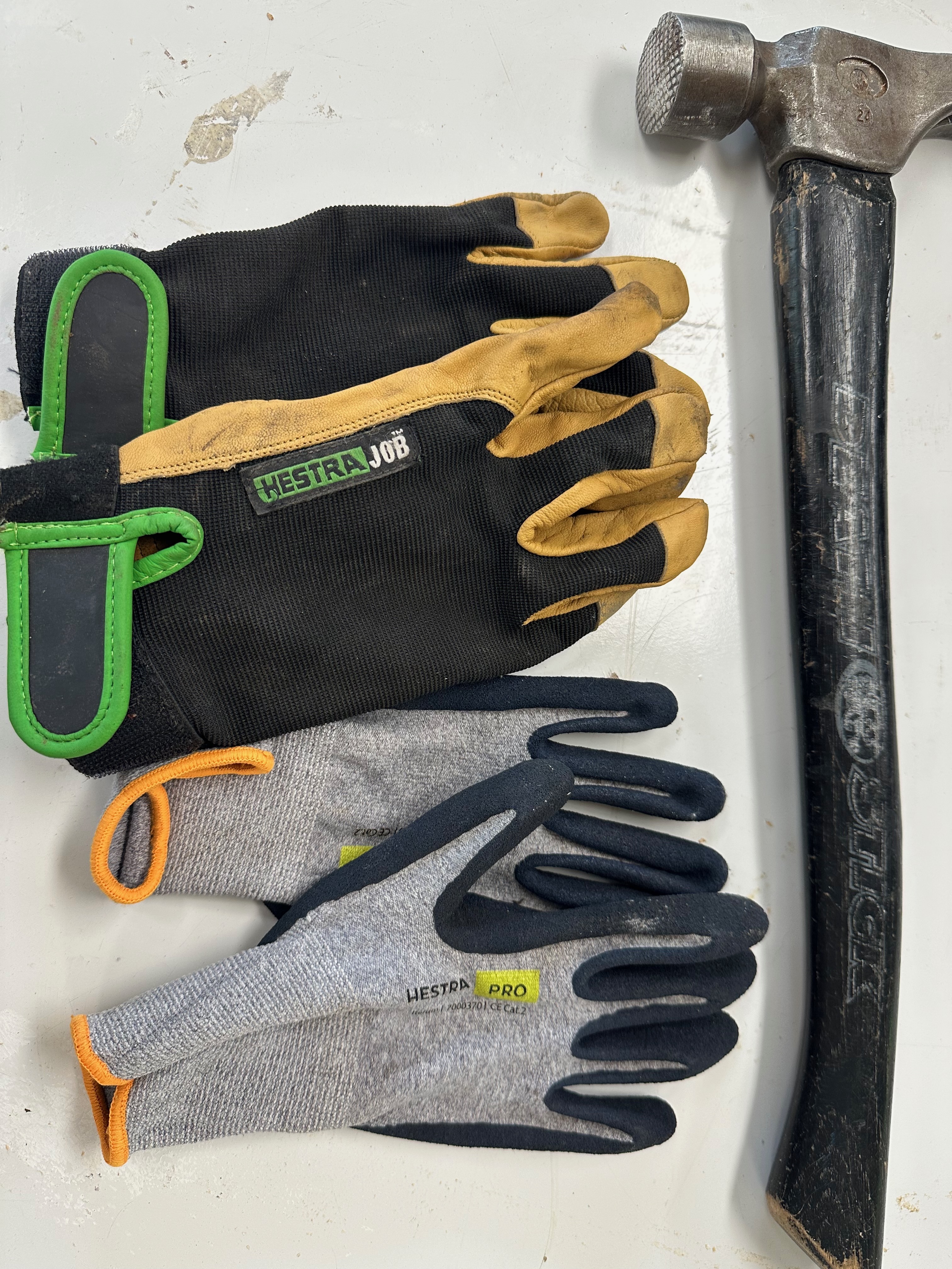 Two pairs of used Hestra work gloves beside a framing hammer.